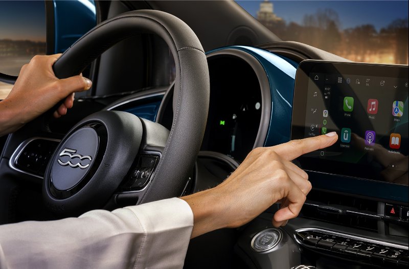 Person using touchscreen in a car with logo on steering wheel.