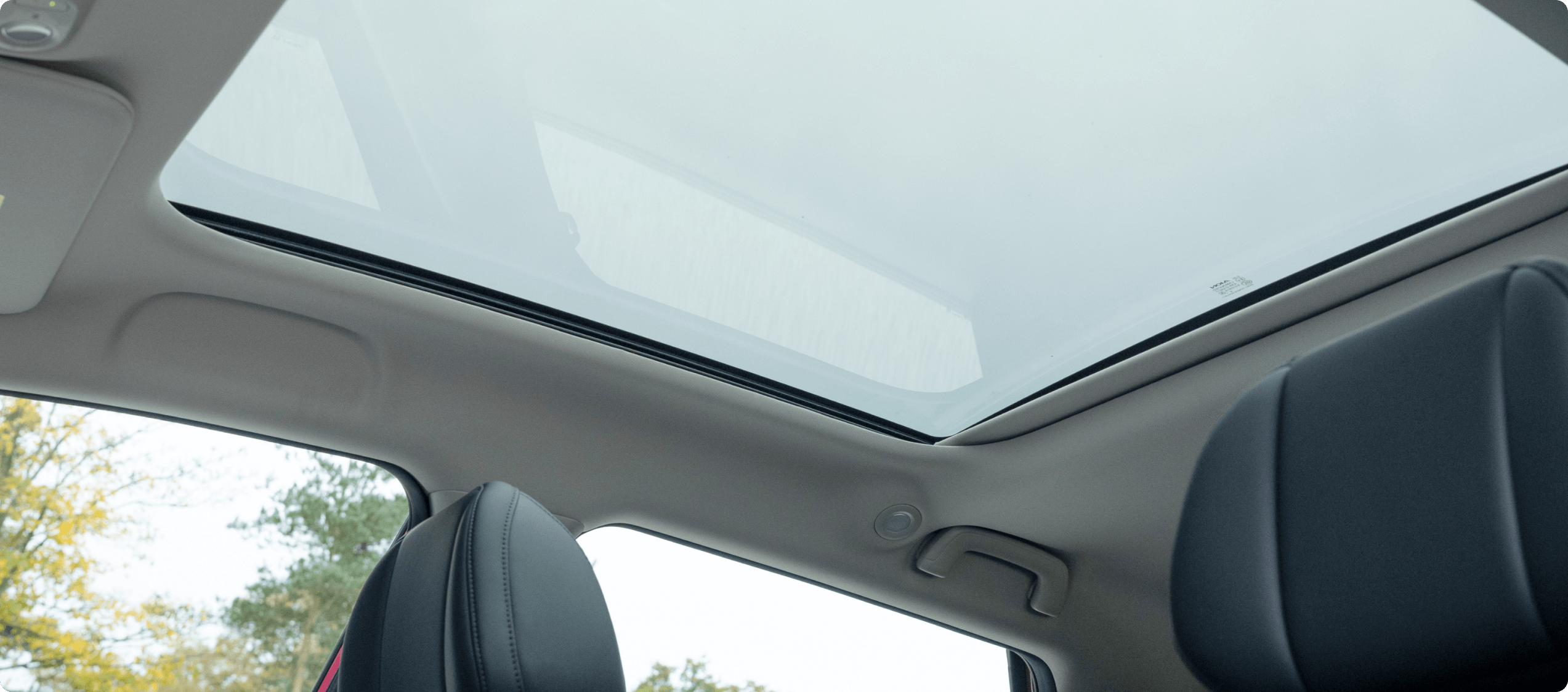 Car interior with panoramic sunroof and part of a black leather seat visible.
