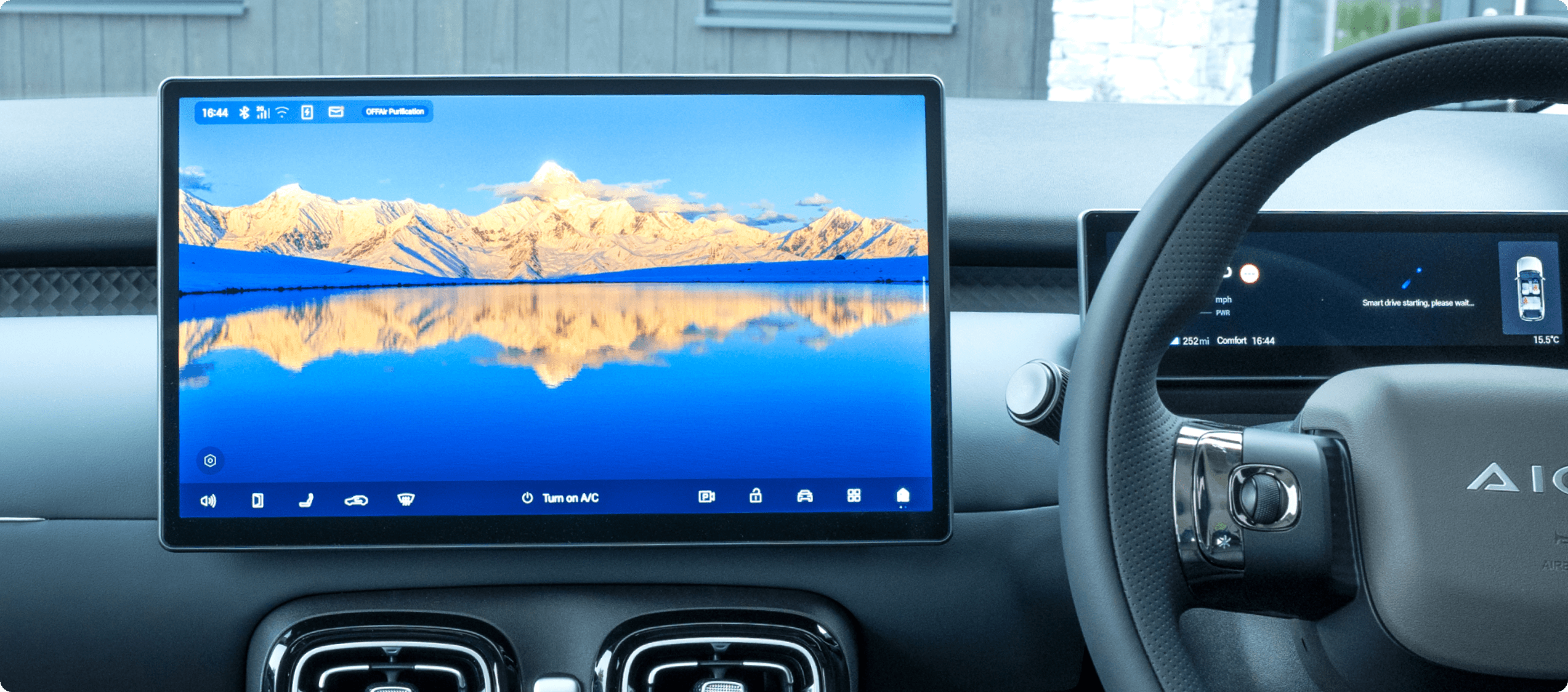 Car dashboard with a central touchscreen displaying a mountain landscape.