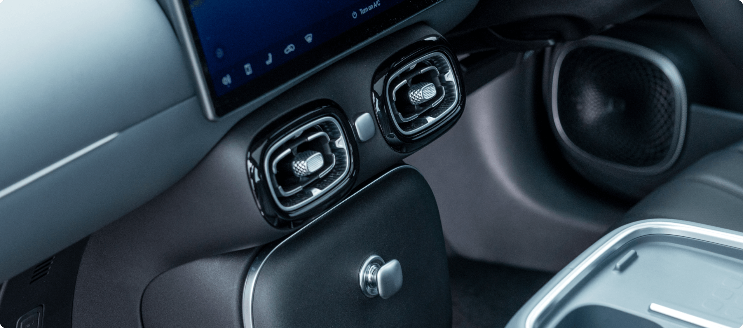 Close-up of a car's interior air vents, part of the dashboard, and a screen.