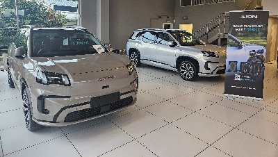 Two Aion vehicles displayed in a showroom with a sign about home charging.