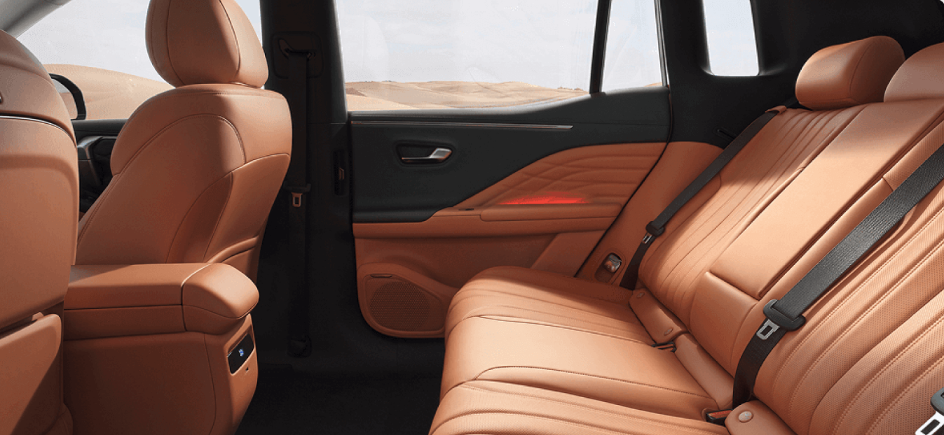 Back seat interior of a car with tan leather upholstery and seatbelts.