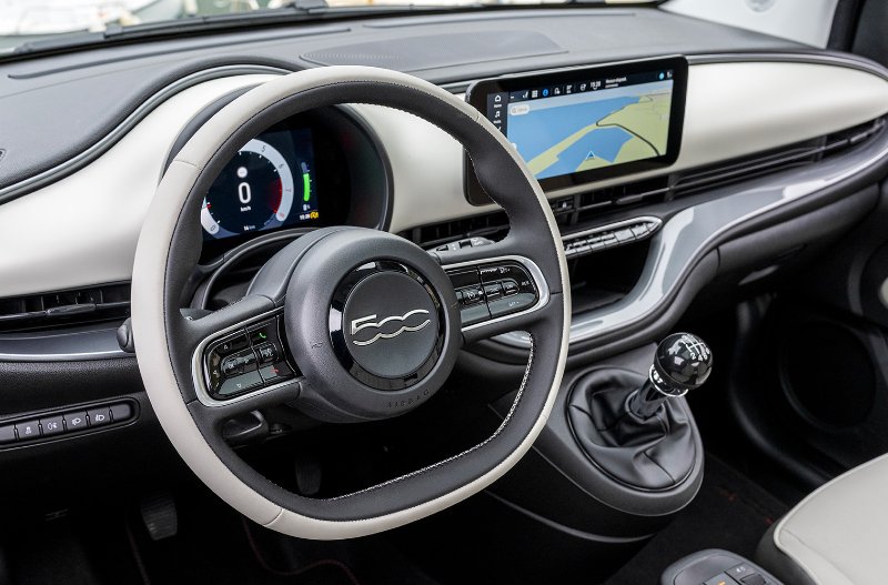 Interior of a car showing steering wheel, digital display, and manual gear stick.