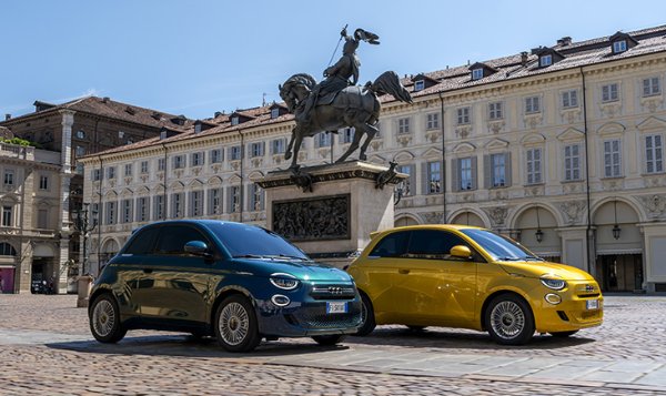 Two compact cars parked in front of a statue in a European square.