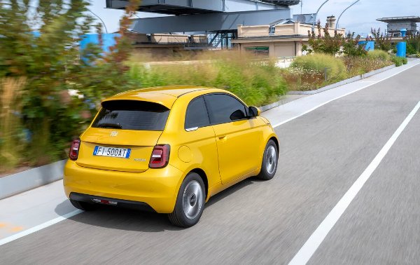 Yellow hatchback car driving on a road, viewed from the rear.