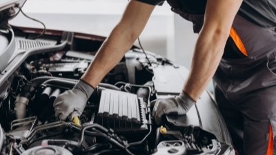 Mechanic inspecting car engine and making notes on a clipboard.